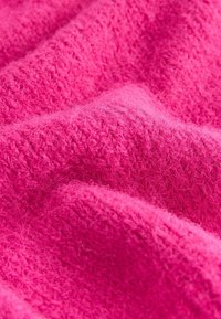 Lys rosa strikket stof med en blød, fuzzy tekstur, der har et vævet mønster og svage variationer i nuancer.