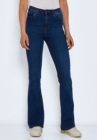 High-waisted, dark blue denim flared jeans with a fitted top and wide lower leg, featuring standard five-pocket design and subtle stitching.