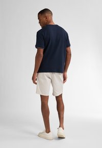 Marineblå kortærmet polo t-shirt med kontraststing, parret med lyse beige shorts og hvide sneakers, set fra bagenden.