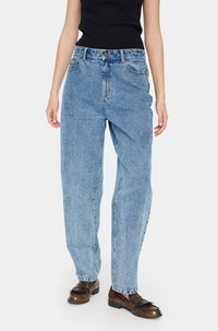 Svijetloplavi traperice s visokim strukom, ravnim nogavicama i izblijeđenom teksturom. Sadrži klasičan dizajn s pet džepova i zatvaranje na metalnu dugmad.