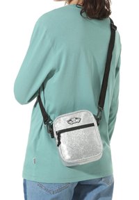 Silver glitter crossbody bag featuring a rectangular shape, black zipper, and adjustable strap. Worn on the side with a mint green top.