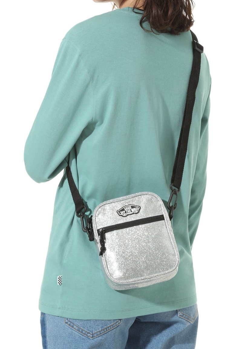 Silver glitter crossbody bag featuring a rectangular shape, black zipper, and adjustable strap. Worn on the side with a mint green top.