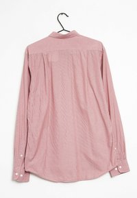 Camisetta a maniche lunghe a righe rosse e bianche con colletto abbottonato, appesa a un gancio. Presenta bottoni sui polsini e un orlo curvo.