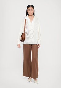White silk blouse with a textured pattern, relaxed fit, paired with brown wide-leg pants and cream-colored slip-on shoes. Brown crossbody bag.