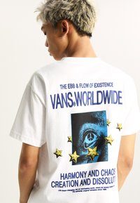 White cotton T-shirt featuring a colorful graphic on the back with stars, an eye illustration, and text in blue and black. Relaxed fit.