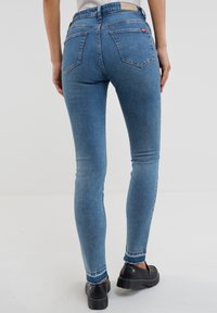 Lieknos mėlynos džinsinės kelnės su nublukusia danga, penkių kišenių dizainu, matomu siuvimu ir prekinio ženklo etikete ant juosmens.