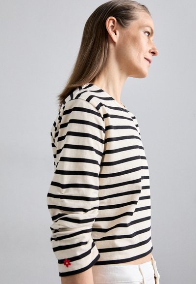 Striped long-sleeve top in cream and black cotton, featuring a floral accent in red on the sleeve, with a relaxed fit and round neckline.