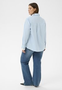 Koszula na guziki w jasnoniebieskie i białe paski, z kołnierzykiem, długimi rękawami i luźnym krojem, zestawiona z niebieskimi, szerokimi spodniami dżinsowymi.