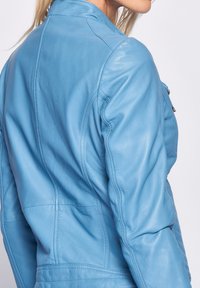 Blaue Lederjacke mit taillierter Passform, sichtbaren Nähten und leicht strukturiertem Finish. Besitzt eine Reißverschlusstasche an der Seite.