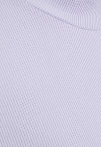 Gros plan d’un tissu tricoté côtelé violet clair avec un bord plié, mettant en valeur la texture et de fines lignes verticales.