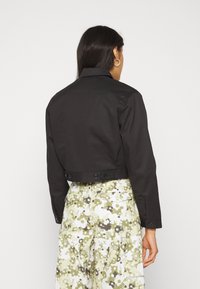 Svart cropped jacka med en strukturerad krage, knappstängningar på baksidan, bärs över mönstrade vida byxor med blommiga mönster i grönt och vitt.