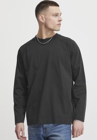 Black long-sleeve shirt with a round neckline and raglan sleeves, paired with blue jeans. Smooth texture, minimal design, and no visible patterns.
