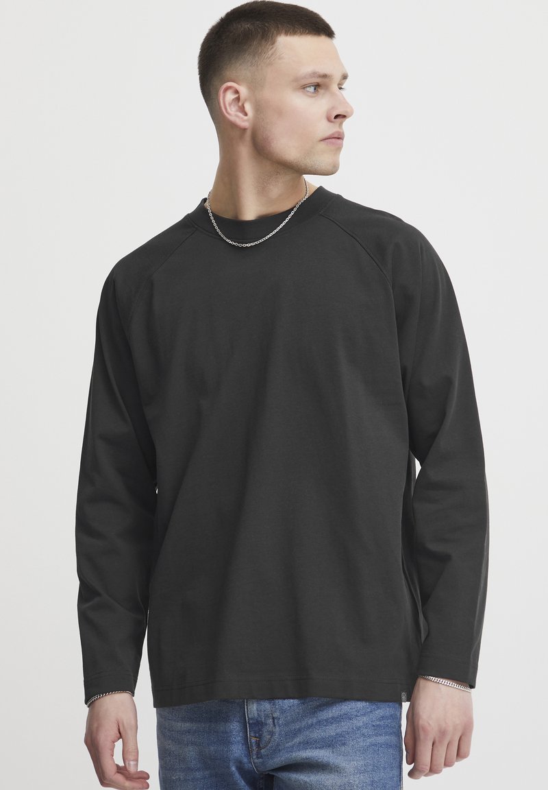 Black long-sleeve shirt with a round neckline and raglan sleeves, paired with blue jeans. Smooth texture, minimal design, and no visible patterns.