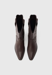 Barna bőrbokalánc csizma hegyes orral, rugalmas oldalpanelekkel és díszítő varrással a szárán. Simas textúra és masszív talp.