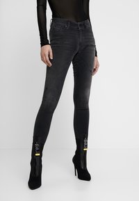 Jeans ajustados de tiro alto en negro con un acabado desgastado y tobillos con cremallera. Combinados con botas negras de tacón alto con un diseño elegante.