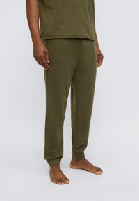 Χακί παντελόνι lounge από μαλακό ύφασμα, με άνετη εφαρμογή, ελαστική μέση και ριμπ μανσέτες. Φορεμένο με γυμνά πόδια.