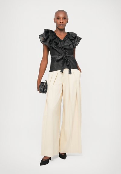 Must mustriga top v-kaelusega, istuv talje ja sidumisdetail, koos kreemjate laiade pükste jaoks; modell hoiab musta kotti.