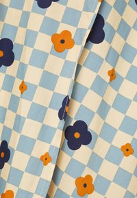 Tecido de algodão com um padrão de tabuleiro de xadrez azul e creme, adornado com motivos florais em laranja e azul escuro. Textura suave com costuras visíveis.