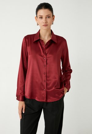 Burgundy satin blouse with long sleeves, button-down front, and a classic collar. Notable smooth texture and slightly curved hem.