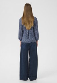Modrá patterned blůza s dlouhými rukávy, spárovaná s volnými, tmavě modrými jeansami. Blůza má texturovaný design a uvolněný střih.
