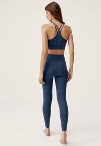 Navy blue aktivwear-set sisältää ristiselän urheiluliivit, joissa on leikkausdetailit, sekä korkea vyötäröiset legginsit, joissa on rei'itettyjä yksityiskohtia jaloissa.