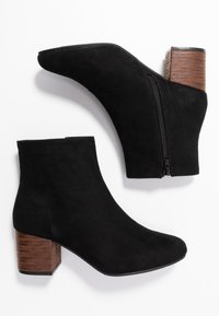 Botines de ante negro con punta afilada, cremallera lateral y un tacón de bloque de madera texturizada. Suela plana y acabado suave.