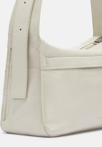 Bolso de mano de cuero color crema con una textura suave, correa ancha y cierre de cremalleras. Presenta costuras horizontales y un detalle de bolsillo en la parte frontal.