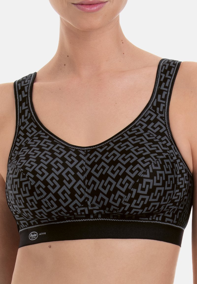 Bras de sport noir avec un motif géométrique gris. Présente des bretelles larges, un col rond et une bande confortable en bas.