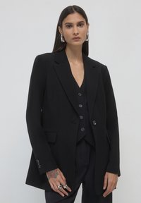 Black blazer with notched lapels, single button closure, and two front pockets. Tailored fit with smooth fabric and subtle texture details.