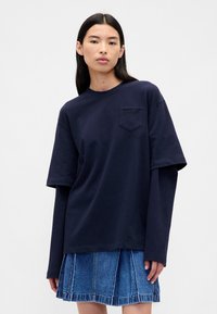 Granatowy, oversize'owy t-shirt z bawełny z krótkimi rękawami, z kieszenią na piersi. Do tego niebieska spódnica jeansowa z pionowymi przeszyciami.