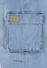 Tejido de mezclilla azul claro con un gran bolsillo trasero que tiene un parche de cuero rectangular etiquetado "Levi Strauss & Co." y detalles de costura visibles.