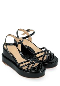 Sandales à plateformes en cuir verni noir avec un talon épais et une bride de cheville. Présente des brides croisées et une finition lisse et brillante.
