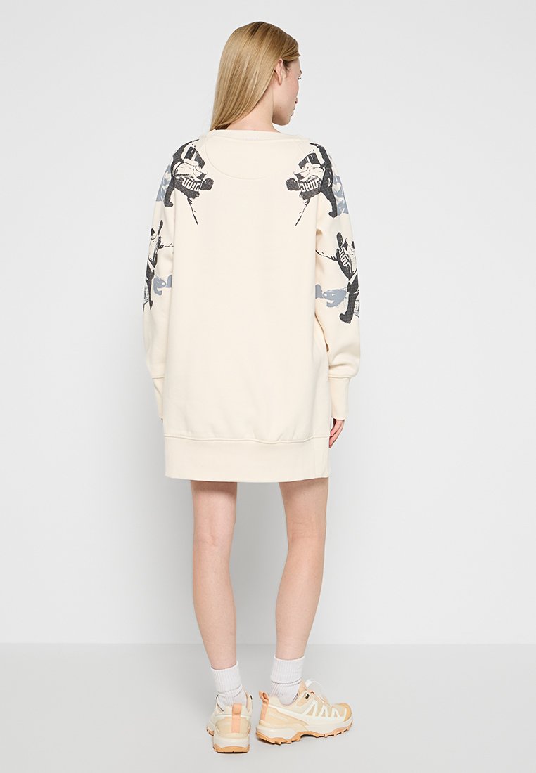 Cremefarbenes, übergroßes Sweatshirt-Kleid mit grauen grafischen Drucken an den Ärmeln, gerippten Bündchen und einem gesäumten Saum. Lässige, lockere Passform.