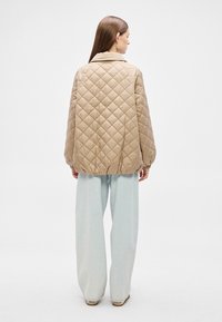 Μπεζ καπιτονέ μπουφάν με γιακά, άνετη γραμμή, ελαστικά μανσέτες και τελείωμα. Φοράται πάνω από ανοιχτό μπλε τζιν παντελόνια με φαρδύ πόδι. Λείο υλικό, μίνιμαλ σχεδιασμός.