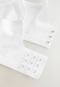 Witte stoffen kleding met verstelbare bandjes, met meerdere haak-en-oogsluitingen aan één kant en een gladde, gestructureerde oppervlakte.