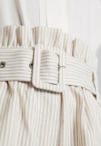 Tessuto a strisce beige e bianche con una vita arricciata e una fibbia rettangolare. Materiale testurizzato con accenti in metallo argentato.