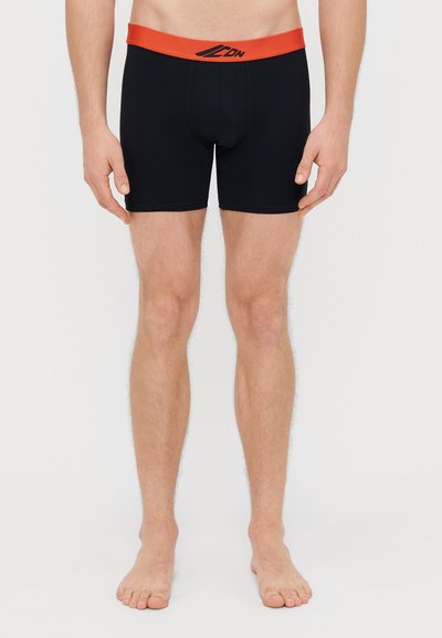 Boxer-briefs noirs avec une large ceinture rouge portant un logo. Le tissu semble lisse et extensible. Design uni, sans motifs visibles.