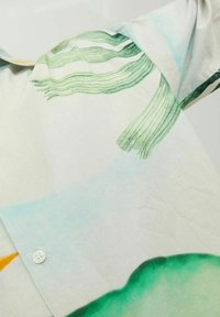 Camicia a maniche corte realizzata in tessuto leggero, con motivi astratti verdi e blu e un dettaglio con bottone sul colletto.