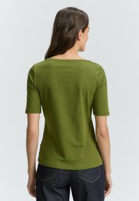 Groene, kortemouwen t-shirt met een brede hals en een comfortabele pasvorm, gemaakt van zachte jersey stof. Draagt met donkere spijkerbroek.