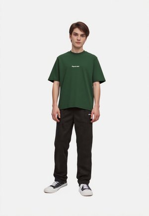 Green short-sleeve t-shirt with a crew neck and white text. Paired with black pants and black sneakers with white accents. Simple design.