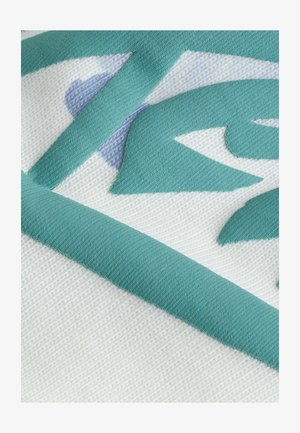 Strukturovana tkanina v bežični barvi z abstraktnimi vzorci v teal in svetlo modri barvi, ki ima trden teal rob. Približan posnetek dizajna.