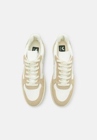 Sneakers med ett vitt läderöverdrag och beige mockadetaljer, perforerat tåparti och platta snören. Logotyp synlig på tungan.