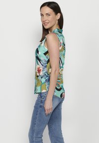 Bezgamelis gėlėtas topas su ryškiais žaliais, mėlynais ir geltonais raštais. Pagamintas iš lengvos medžiagos, turi apykaklę ir laisvą siluetą.