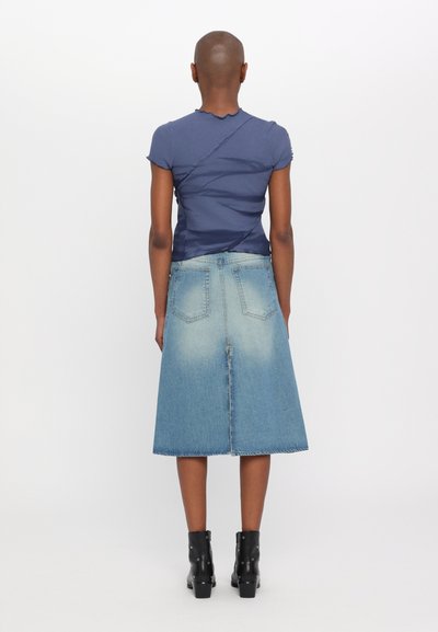 Mørkeblå tætsiddende t-shirt med struktureret overflade og scalloped halsudskæring, parret med en lyseblå denimnederdel, der ender ved midten af læggen, og sorte ankelstøvler.
