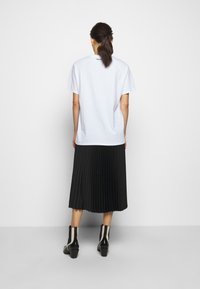 Bílý oversized tričko s kleslými rameny, spárované s černou plisovanou sukní a černými kotníkovými botami s bílými akcenty.