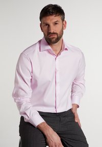 Helles rosa Langarmhemd mit Button-Down-Kragen und hellen Knöpfen. Strukturiert, schmal geschnitten, kombiniert mit grauen gemusterten Hosen.