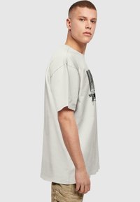Lys grå bomulds t-shirt med korte ærmer, der har et sort grafisk design på forsiden. Løs pasform og rund hals.
