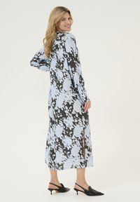 Abito lungo di un azzurro chiaro con motivi astratti in bianco e nero, dotato di maniche lunghe e dettagli con spacco laterale. Tacchi slingback neri.