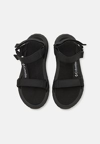 Black sandals featuring a flat sole, adjustable fabric straps, and textured footbed. Branding visible on the insole. Simple and functional design.