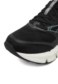 Crni sportski tenisica s prozračnim mrežastim gornjim dijelom, reflektirajućim detaljima i jastučićem bijelog potplata. Ima teksturirani vrh na prstima i sustav vezanja.